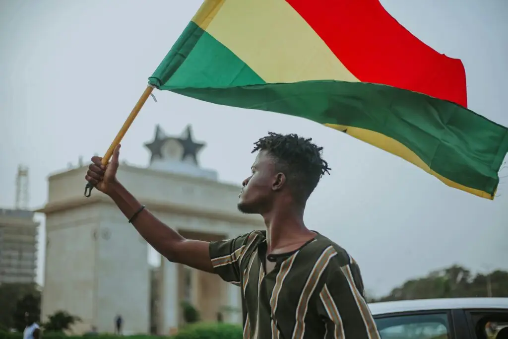 African male with dreadlocks raising flag of Ghana country with colorful stripes while looking away in town Culturally grounded educational consulting